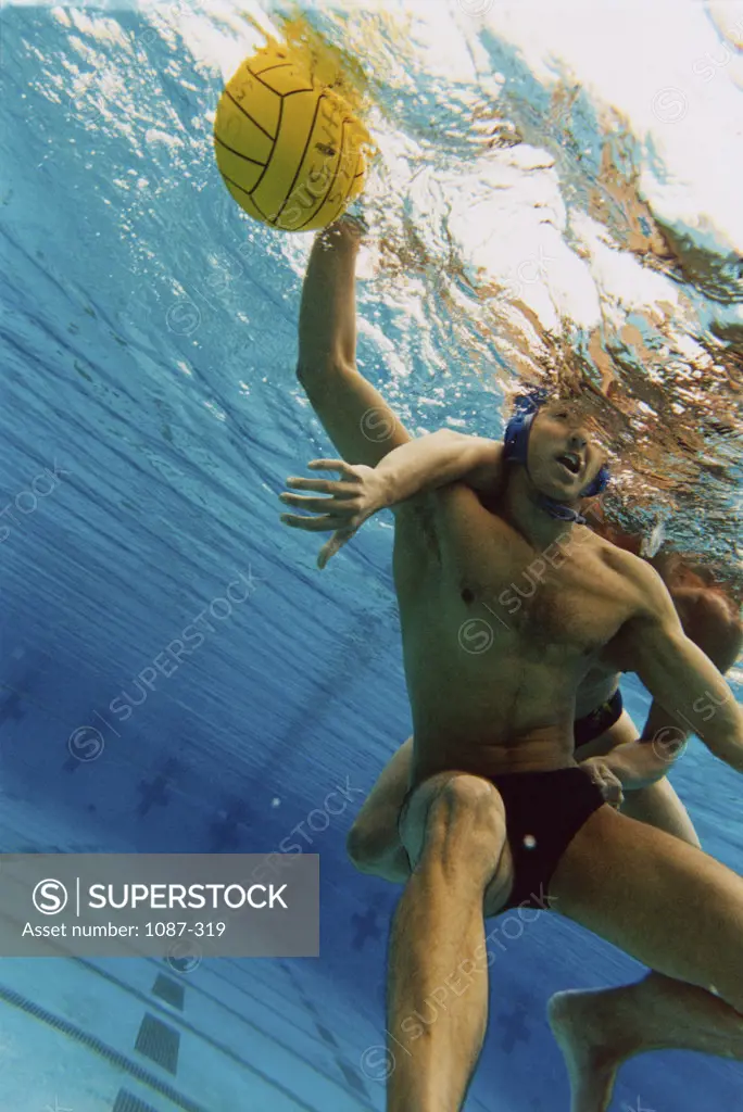Two people playing water polo in a swimming pool