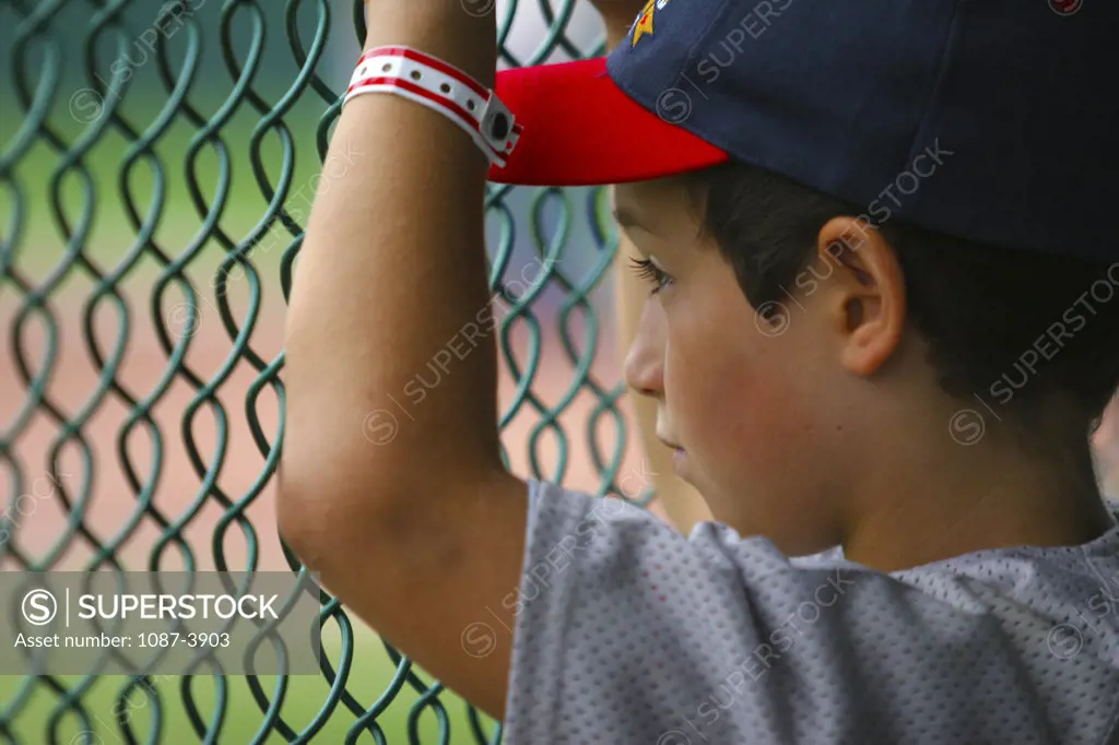 Boy looking at a baseball field through a fence