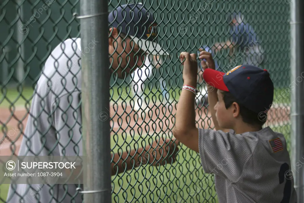 Boy discussing with a baseball player across a chainlink fence