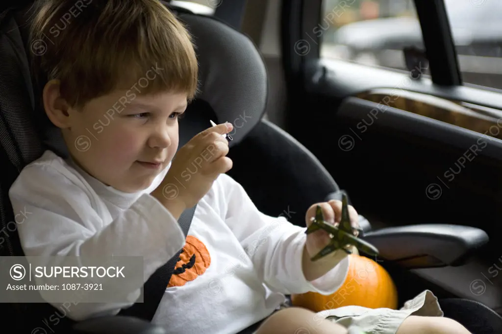 Boy sitting in a car seat playing with a toy airplane