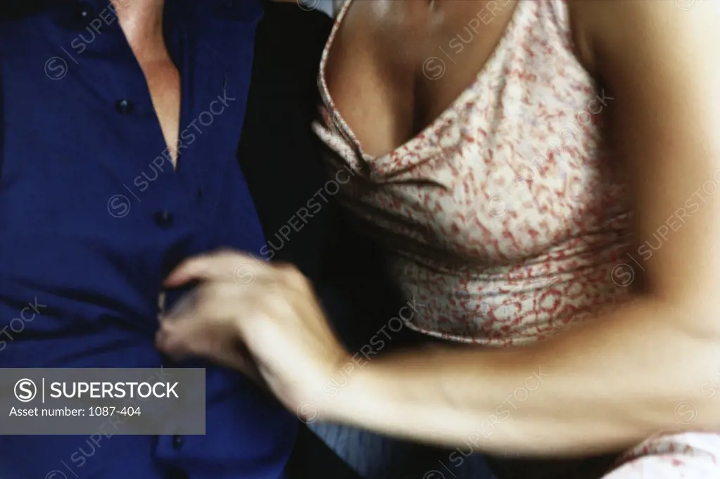 Mid section view of a young woman unbuttoning the shirt of a young man