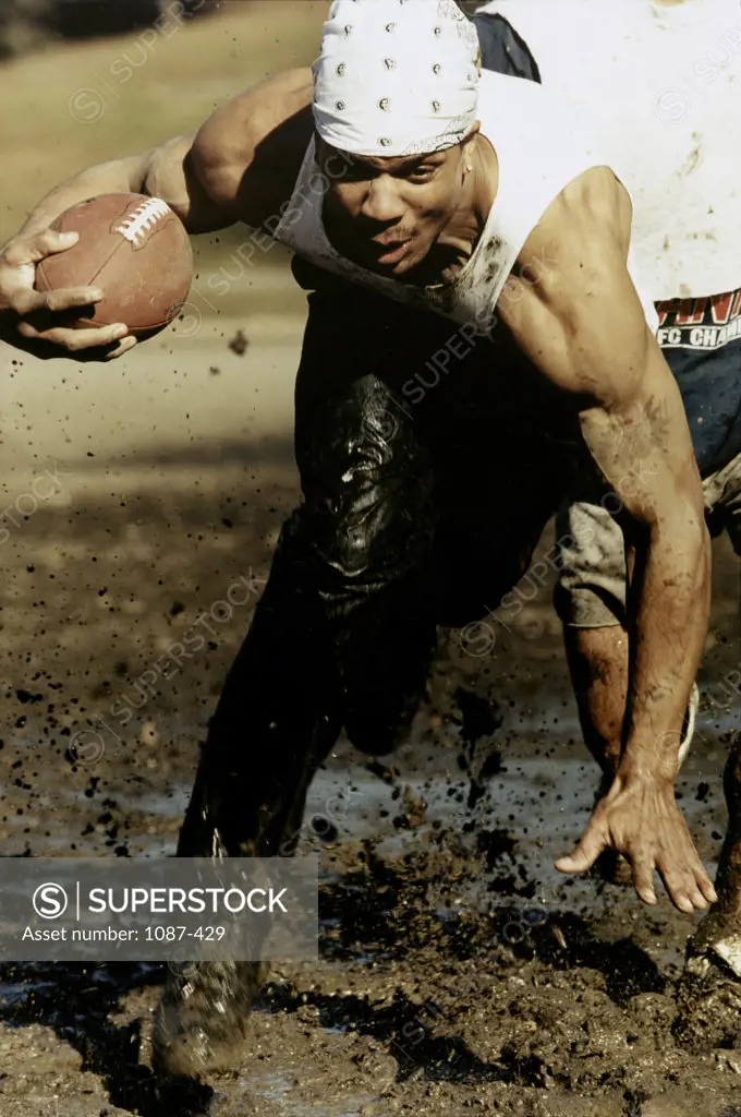 Two young men playing football in a muddy field