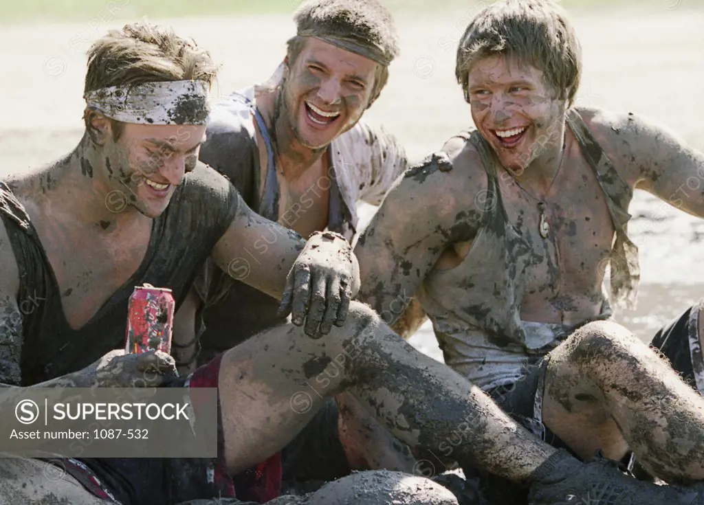 Close-up of three young men covered with mud smiling