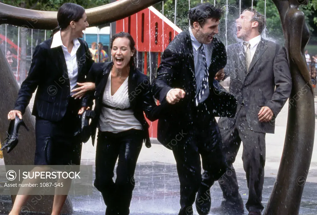Two businessmen and two businesswomen walking through a fountain