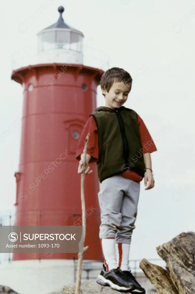 Low angle view of a boy standing in front of a lighthouse holding a stick