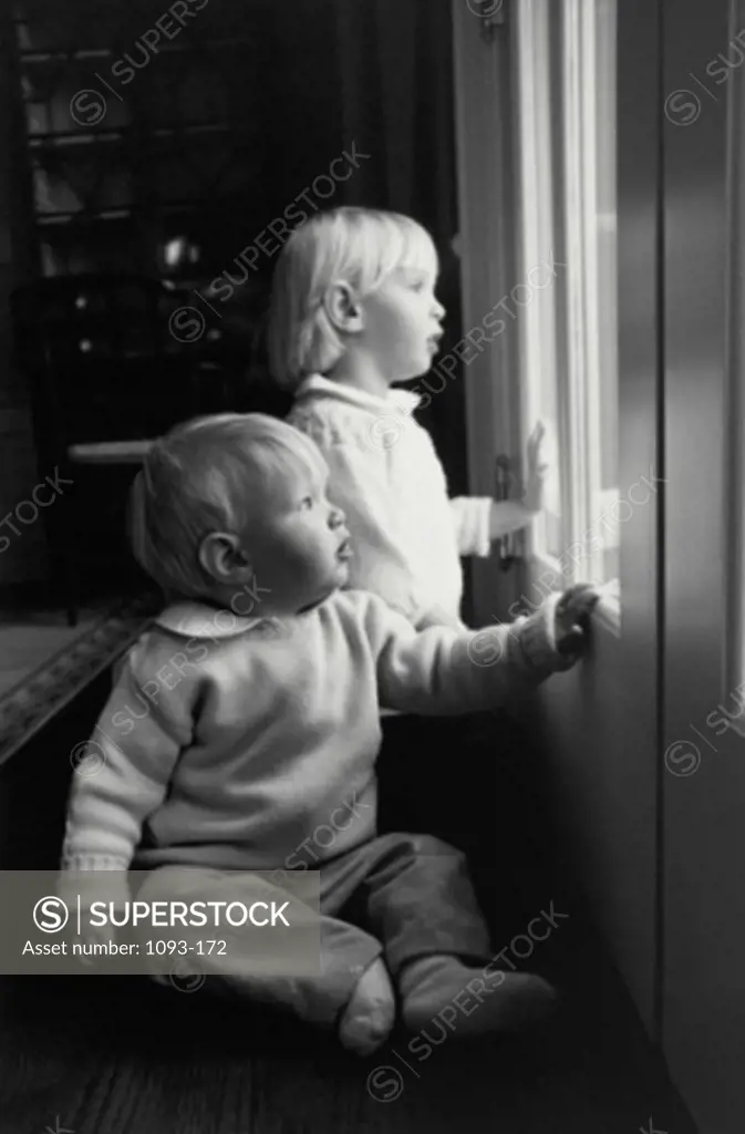 Side profile of a sister with her brother looking through the glass of a door