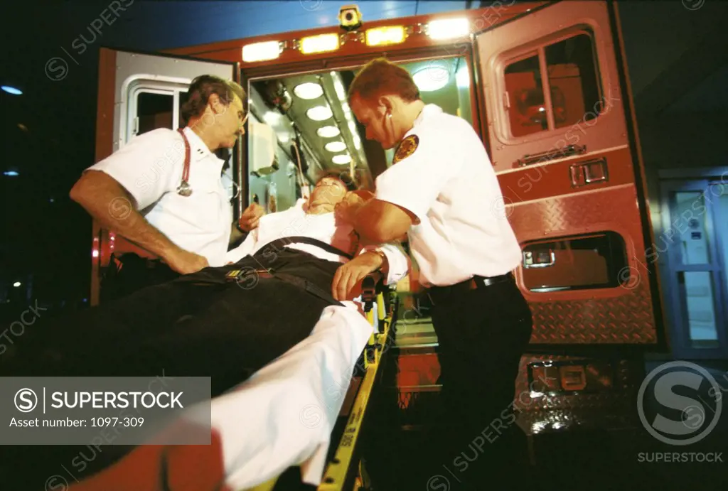 Two paramedics pushing a man on a stretcher into an ambulance