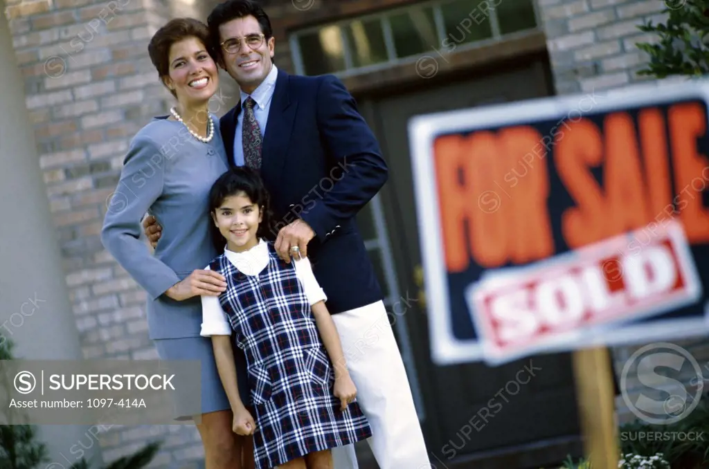 Portrait of parents and their daughter standing in front of their new home