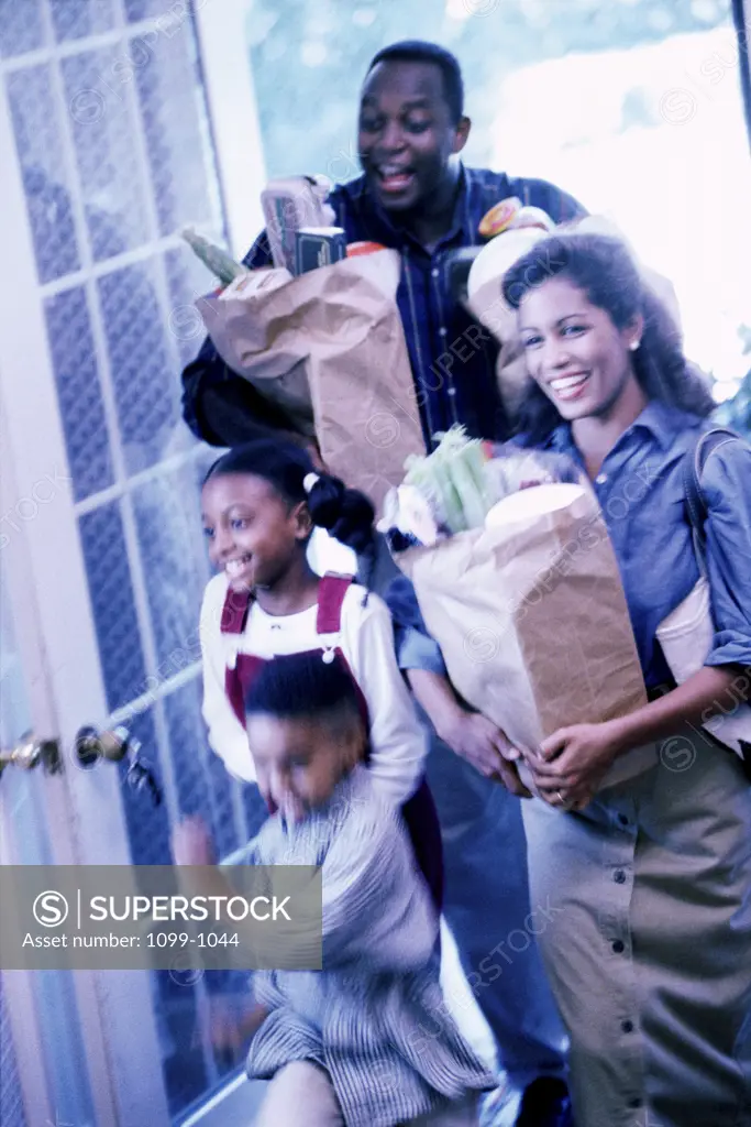 Family entering their home carrying shopping bags