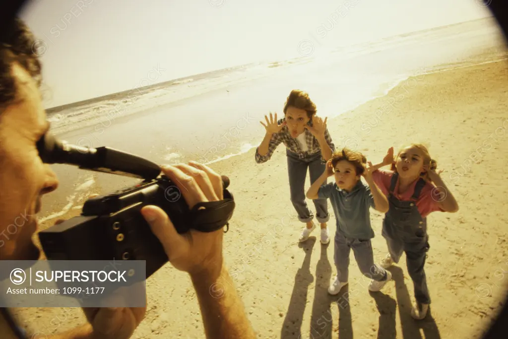 Father filming his wife and children on the beach