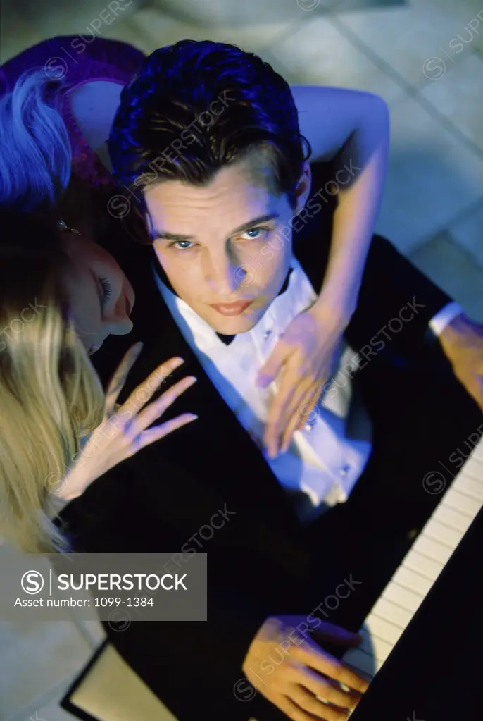 Portrait of a young man playing the piano with a young woman hugging him