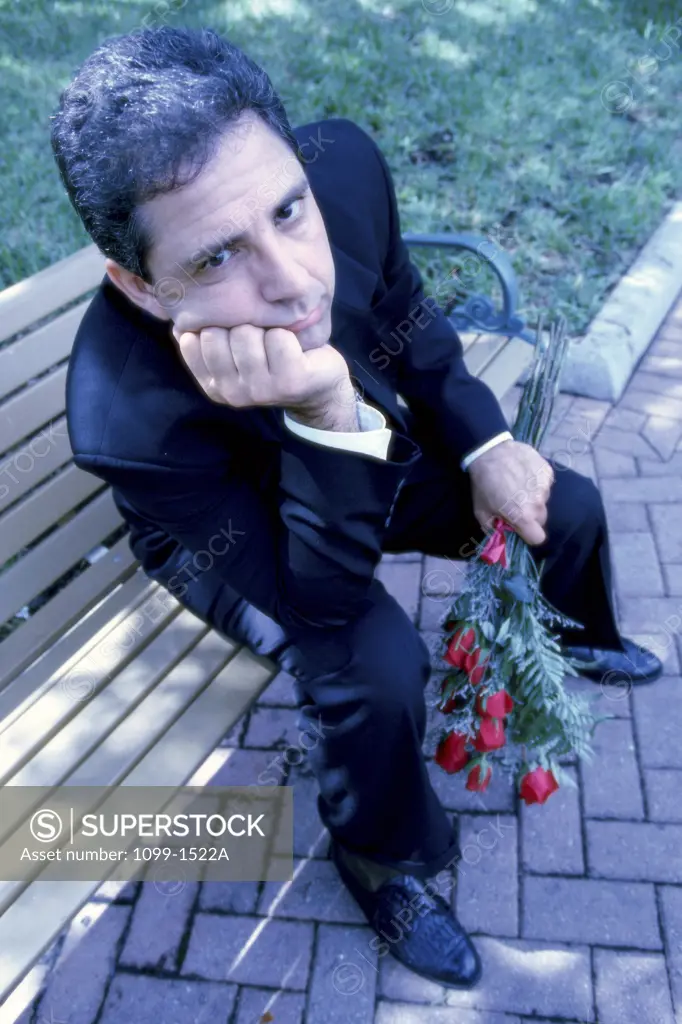 Portrait of a mid adult man sitting on a park bench holding a bouquet of flowers