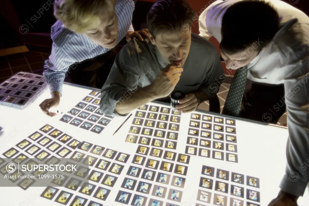 Two mid adult men and a mid adult woman looking at slides