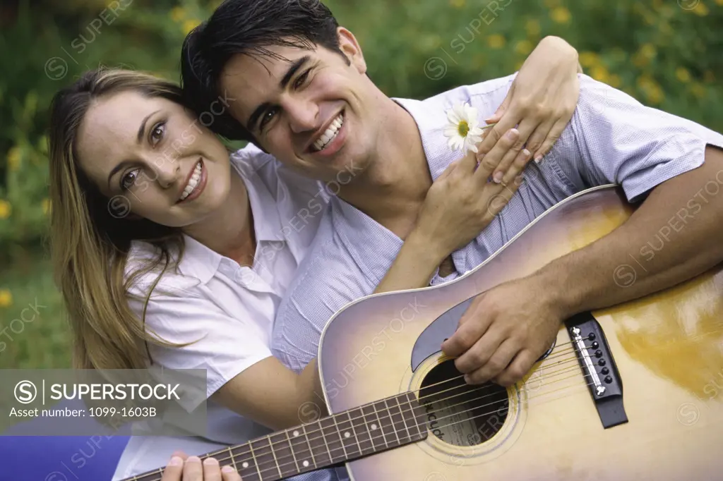 Young man playing the guitar with a young woman sitting beside him