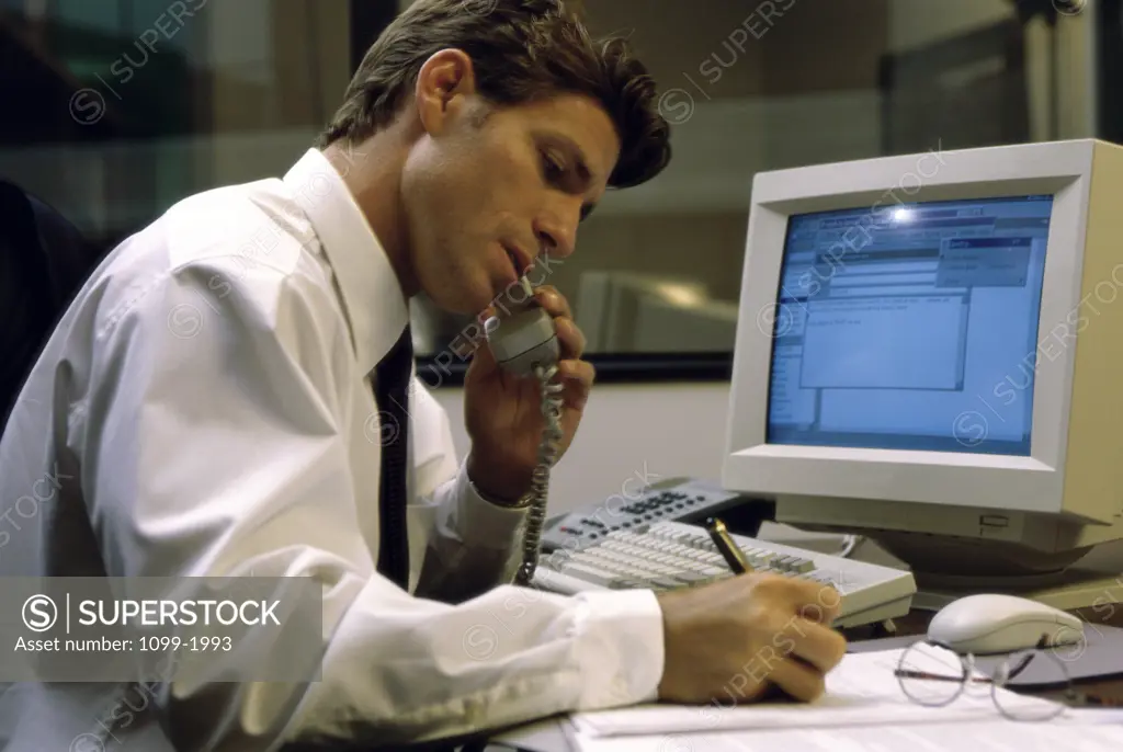 Side profile of a businessman writing and talking on the telephone