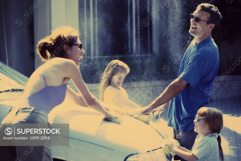 Parents washing the car with their two daughters