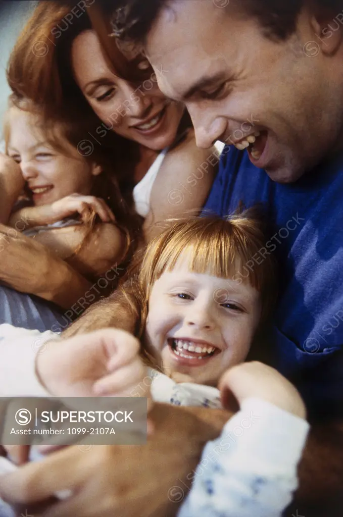 Close-up of a mid adult couple hugging their daughters and smiling