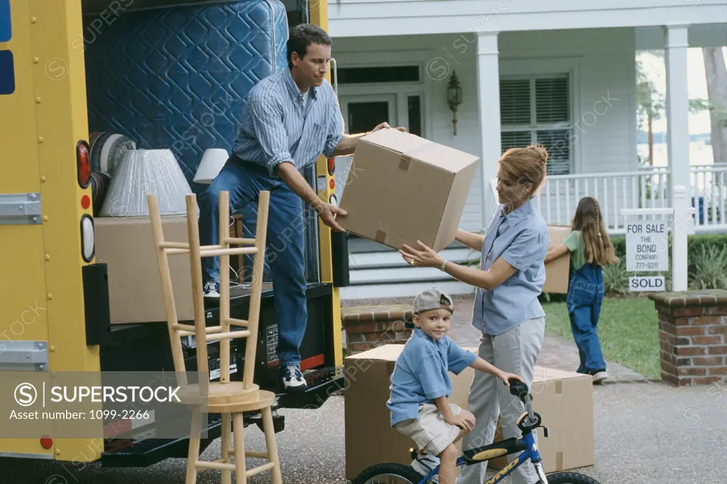 Side profile of a mid adult couple unloading a van with their son riding a bicycle near them