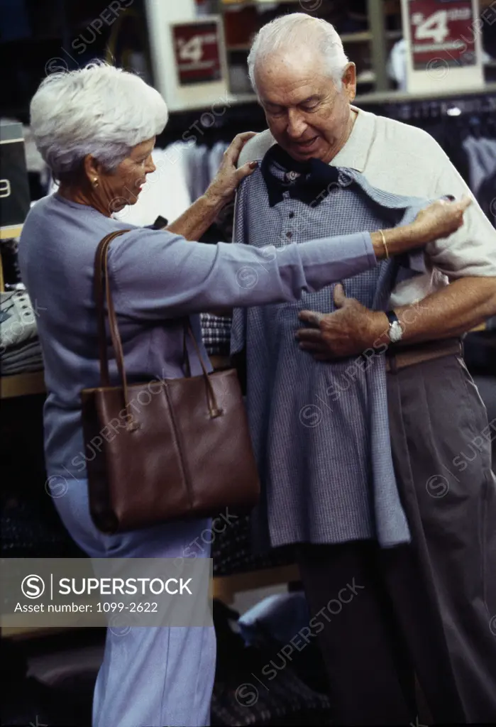 Side profile of a senior woman holding a polo shirt in front of a senior man in a clothing store