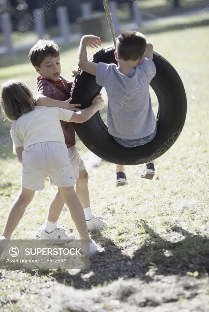 Two boys and a girl paying on a tire swing