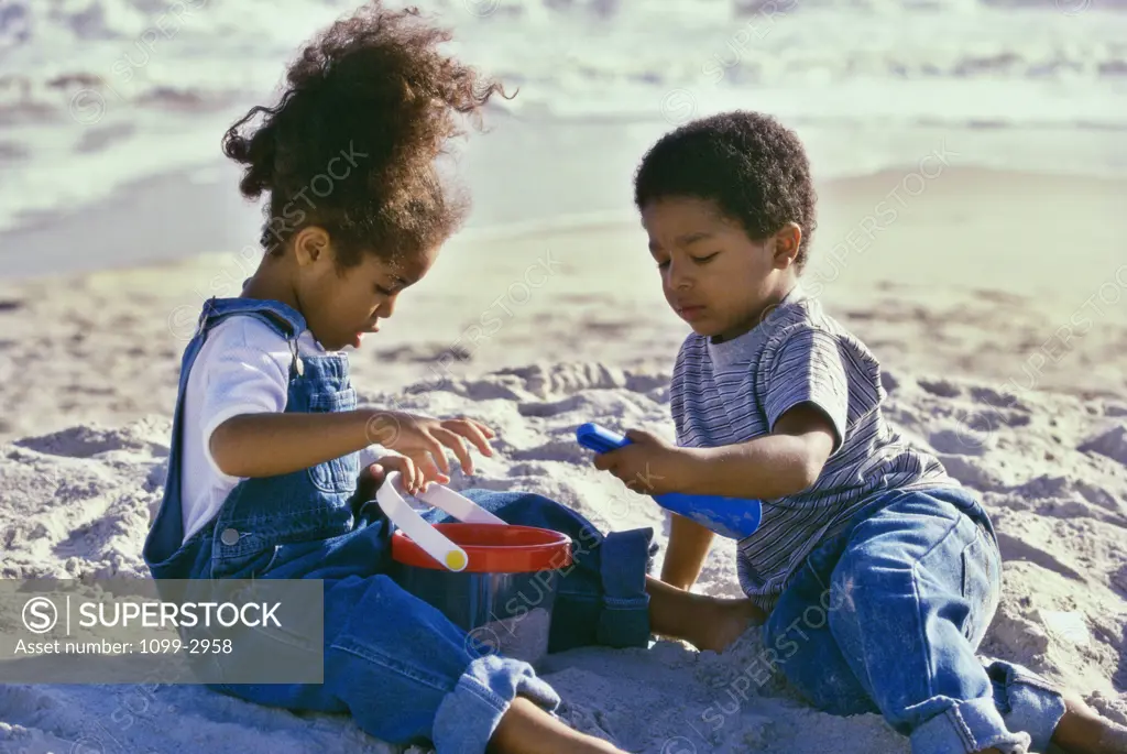 Boy and a girl playing with a sand pail and a shovel on the beach