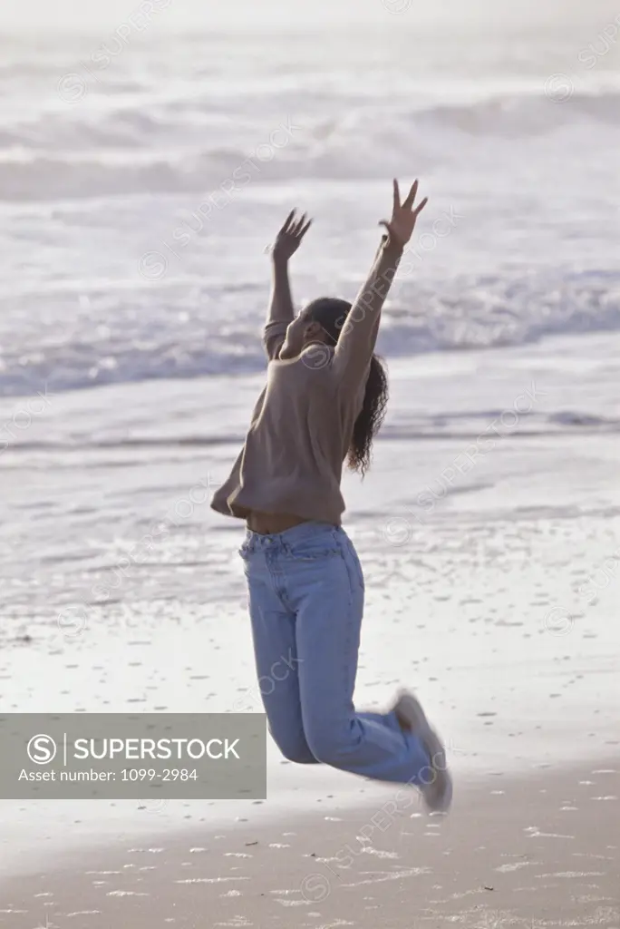 Side profile of a young woman jumping on the beach