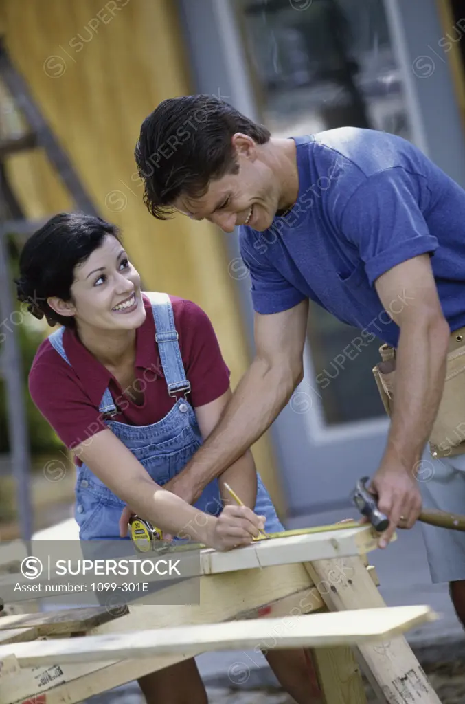 Mid adult couple measuring a wooden board with a measuring tape