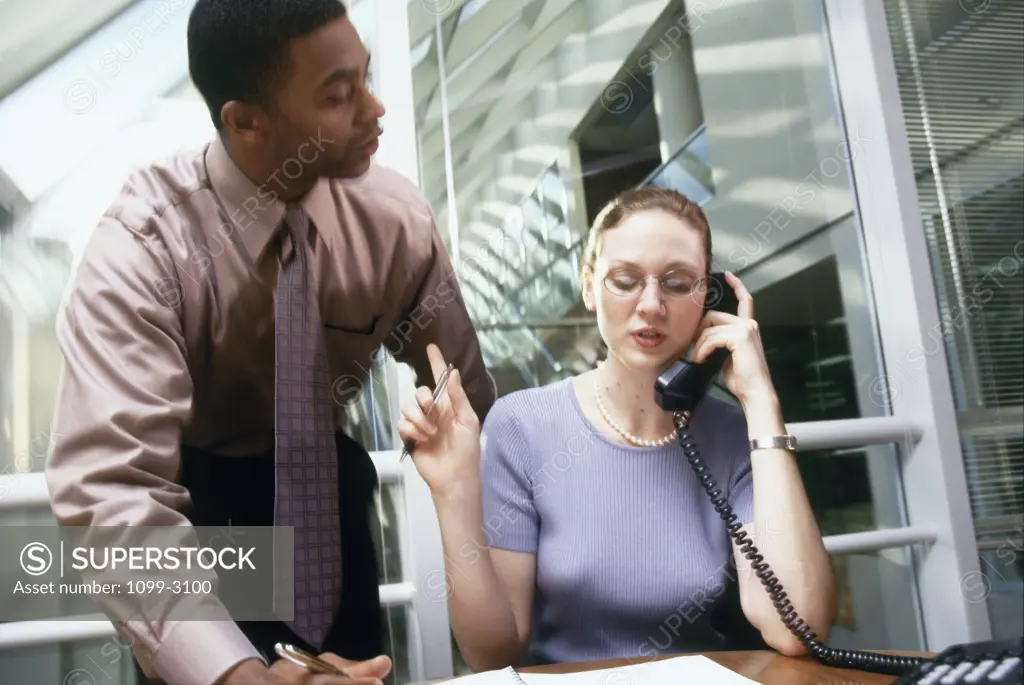 Businesswoman talking on the phone and a businessman standing behind her