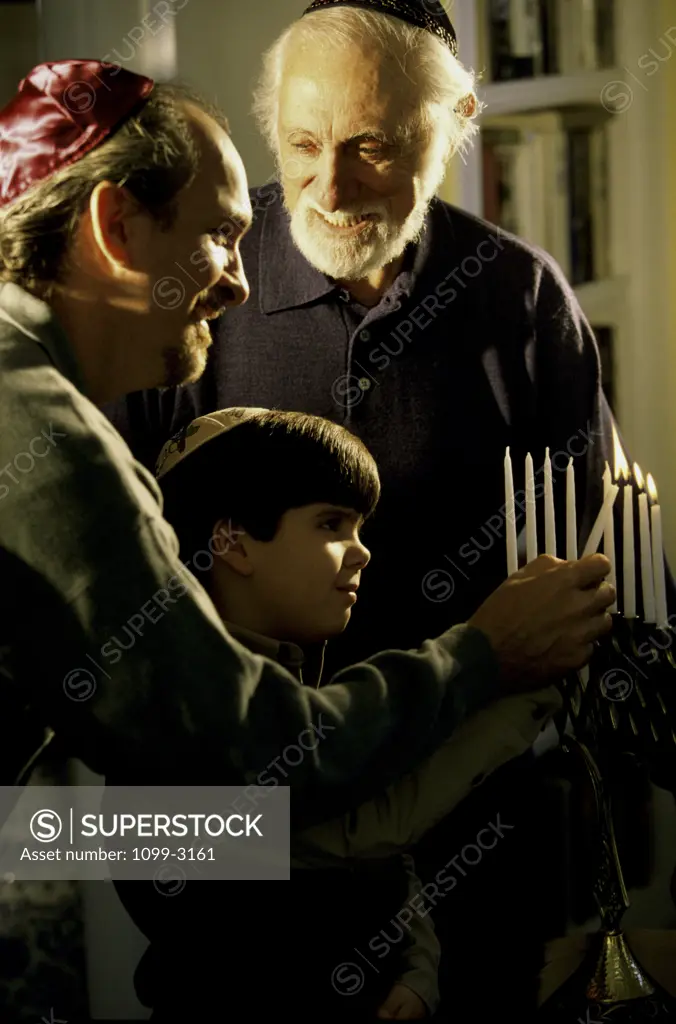Grandfather standing with his son and grandson lighting candle on a menorah