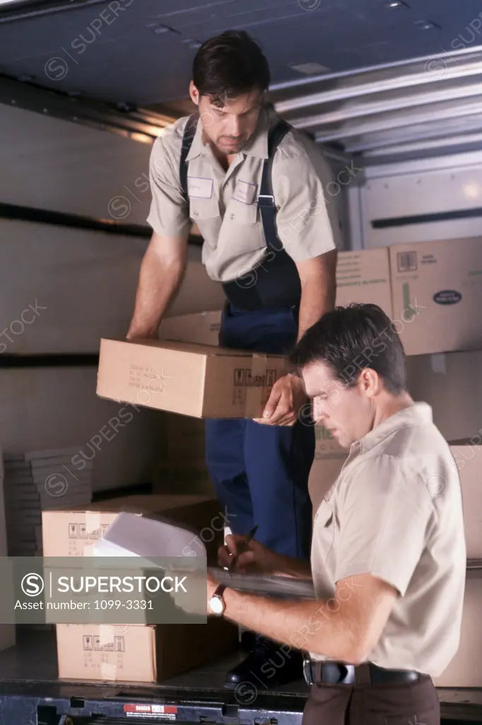 Mid adult man writing on a clipboard with another mid adult man holding a cardboard box beside him