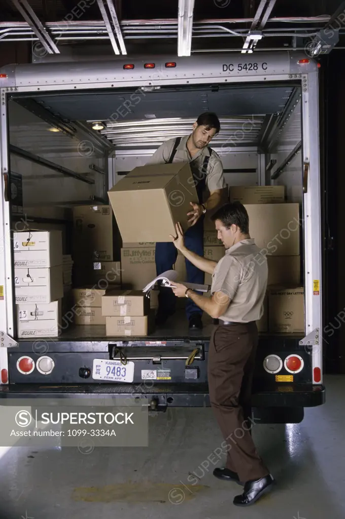 Two mid adult men unloading cartons from a truck