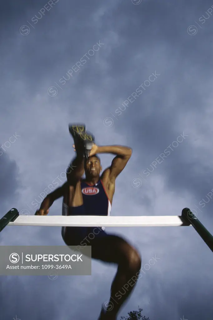 Low angle view of a young man jumping over a hurdle