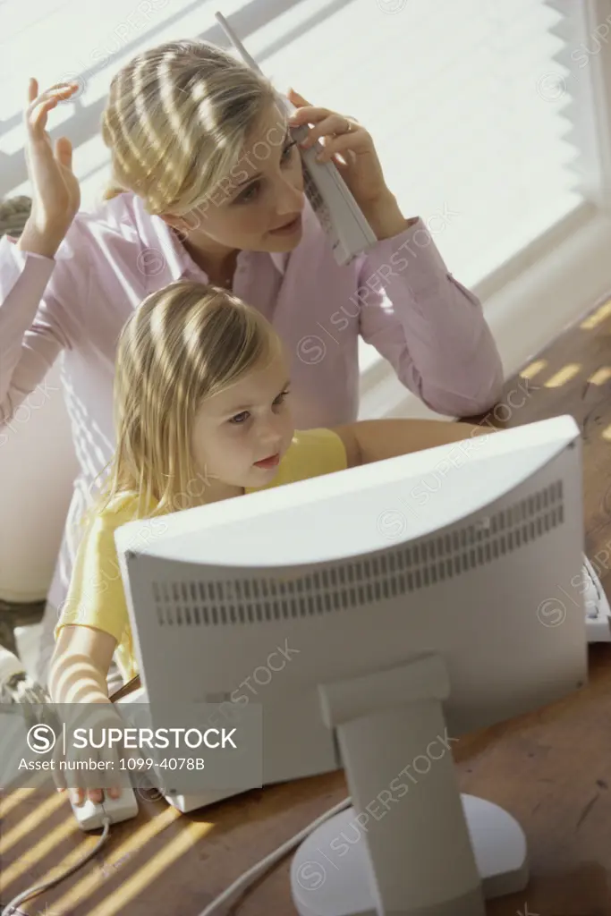 Young woman talking on a cordless phone and her daughter using a computer