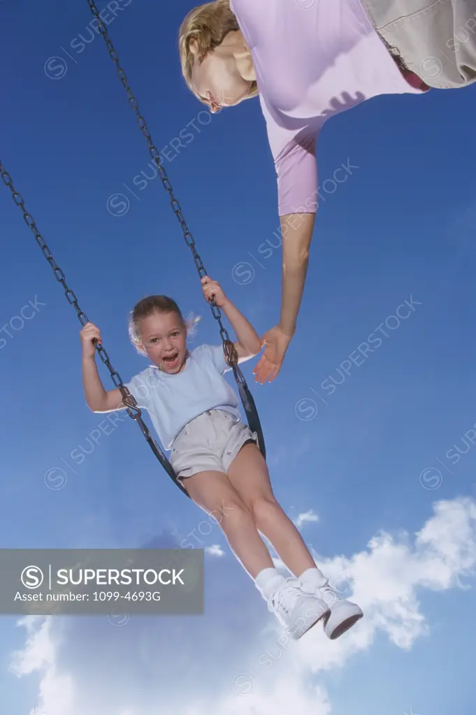 Low angle view of a mother pushing her daughter on a swing