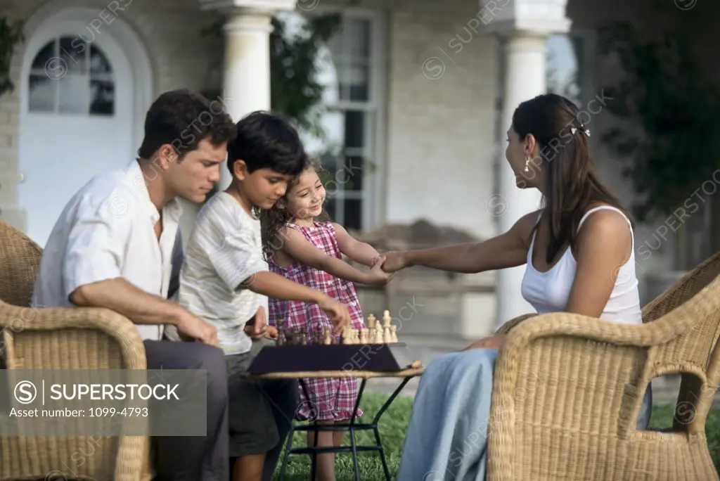 Side profile of a mid adult couple sitting in armchairs with their children playing chess