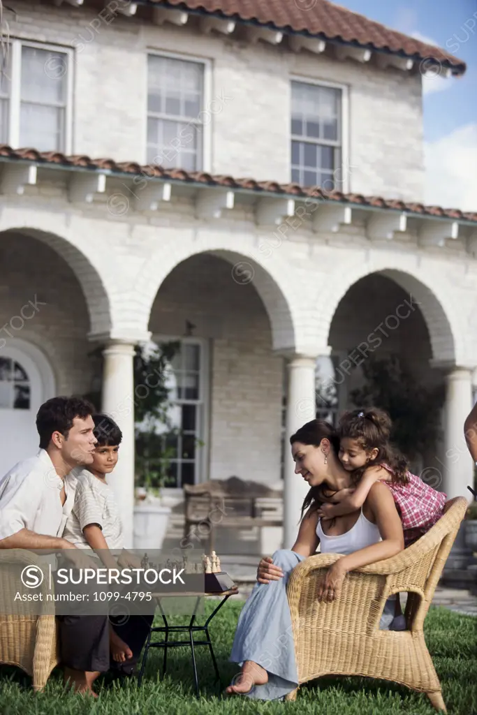 Side profile of a mid adult couple sitting in armchairs with their children playing chess