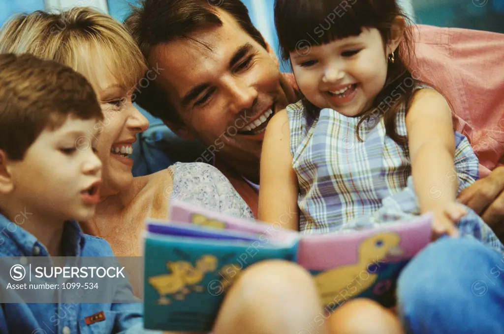 Close-up of a mid adult couple reading a picture book with their son and daughter