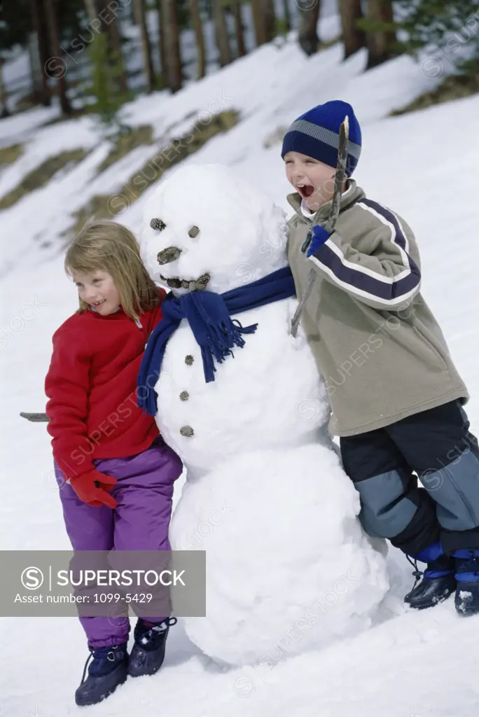 Boy and a girl standing beside a snowman