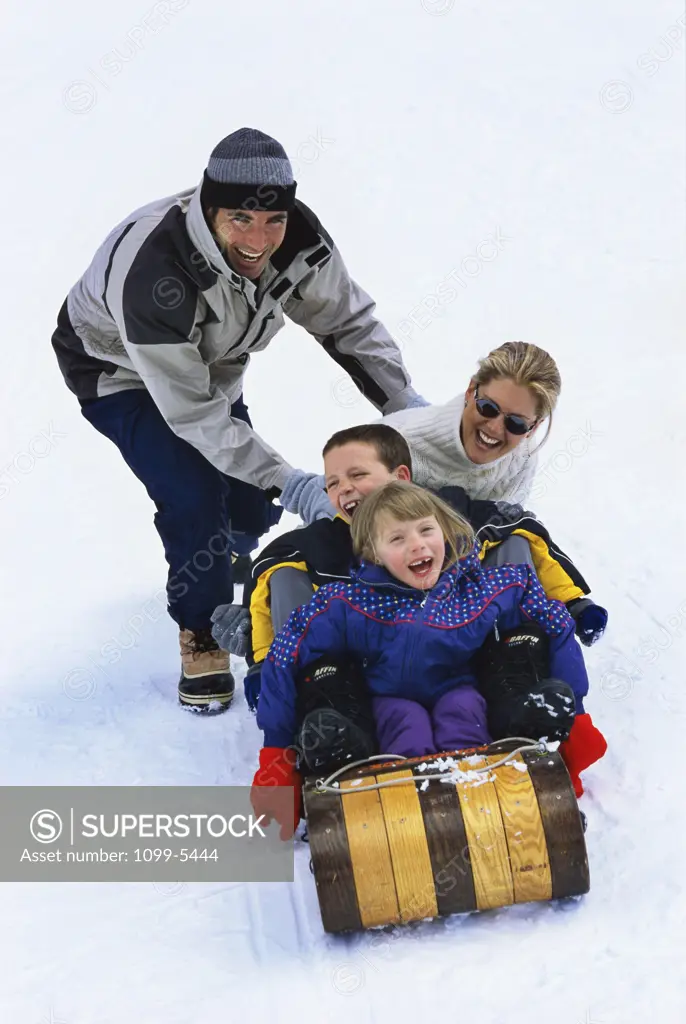 Mid adult man pushing a mid adult woman and his two children on a sled