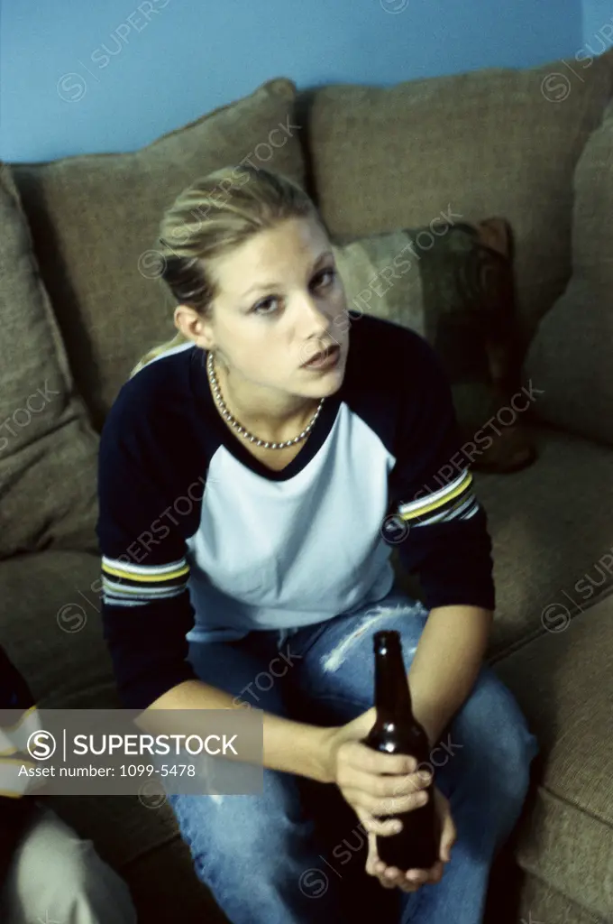 Portrait of a teenage girl sitting on a couch holding a bottle of beer