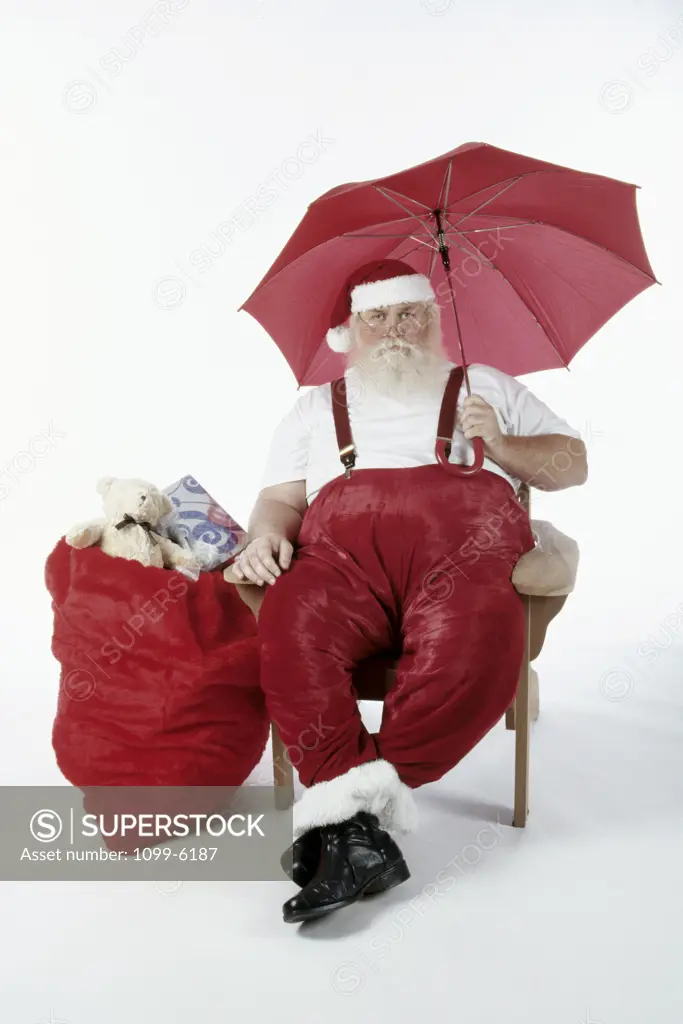 Santa Claus sitting in a chair and holding an umbrella