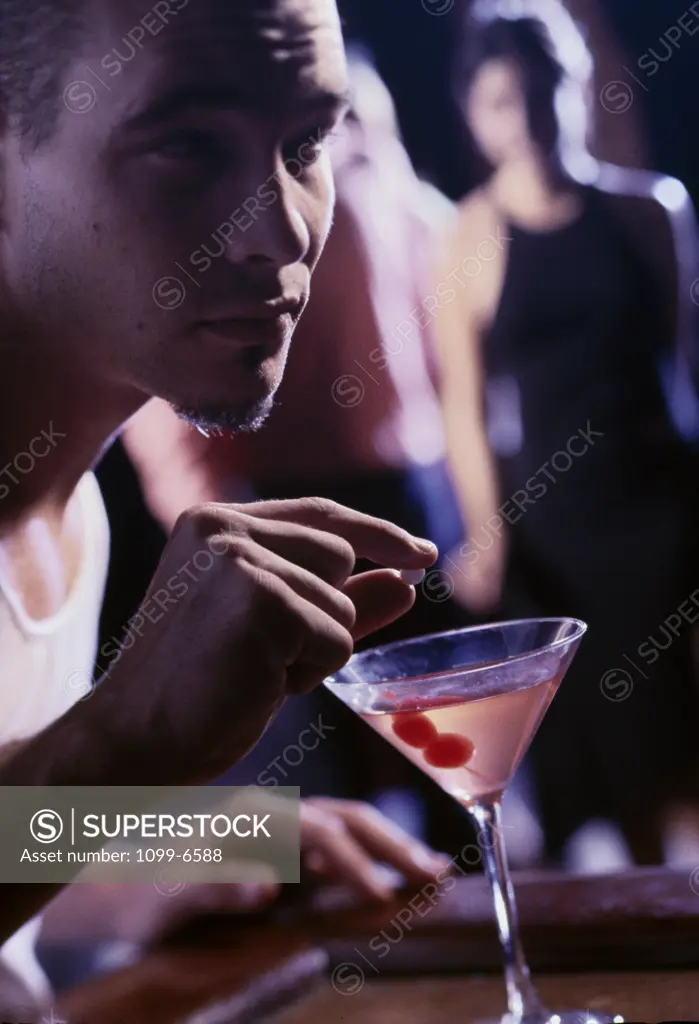 Close-up of a mid adult man putting a pill into a martini