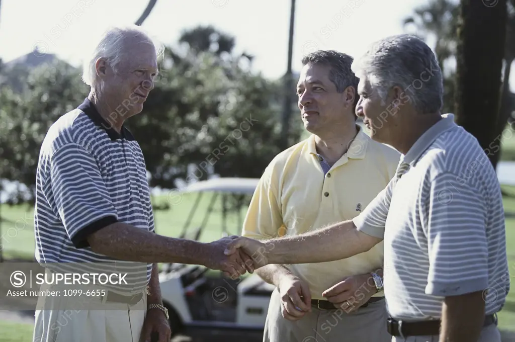 Close-up of three senior men shaking hands on a golf course
