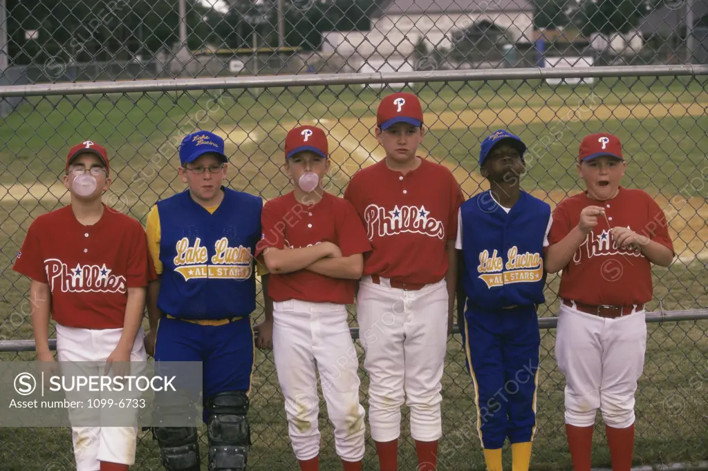 Group of boys on a baseball team standing against a chain-link fence