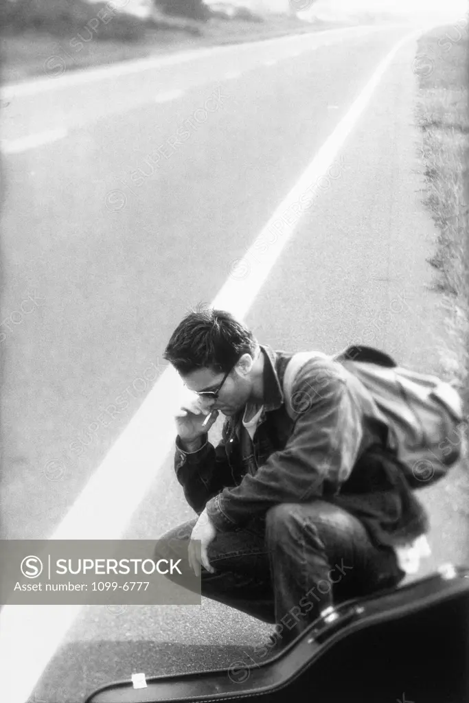 Side profile of a young man squatting on the road smoking a cigarette