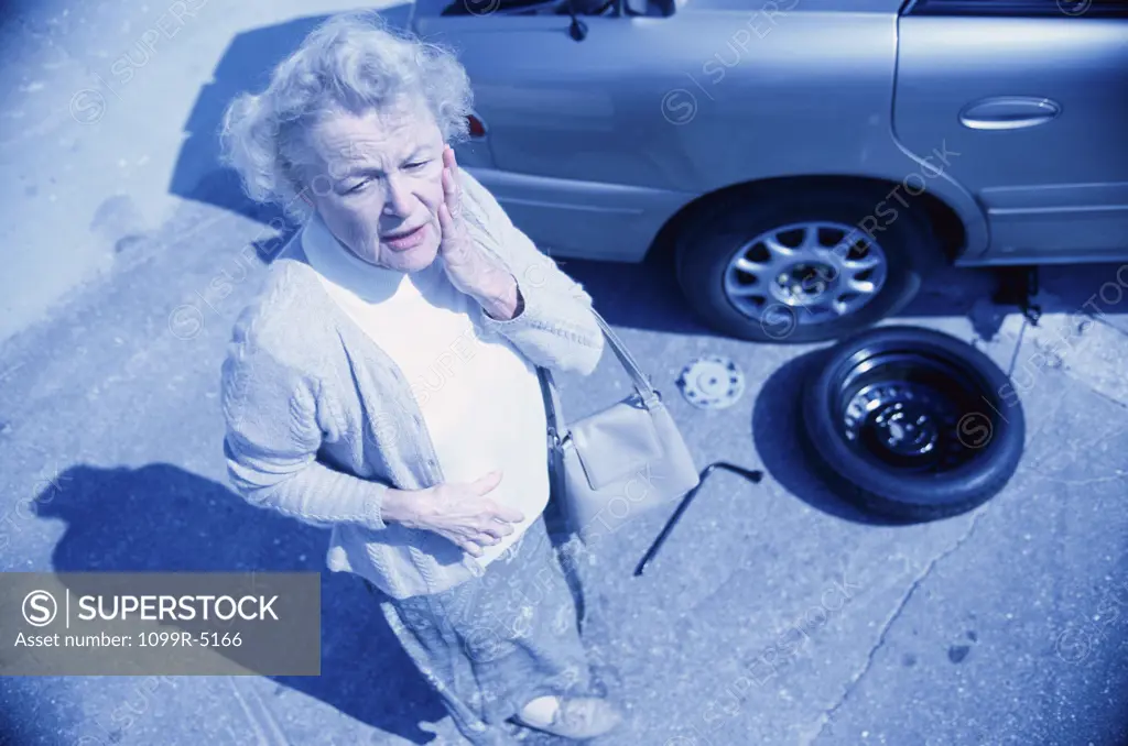 Senior woman standing beside a broken down car