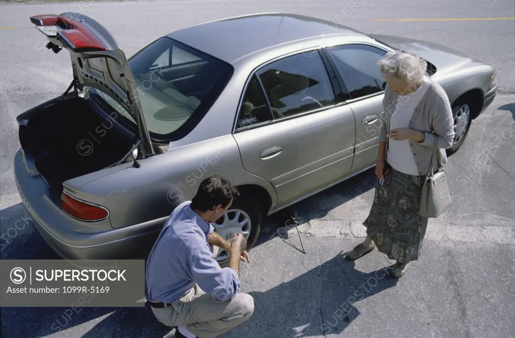 Mid adult man helping a senior woman change a flat tire on her car