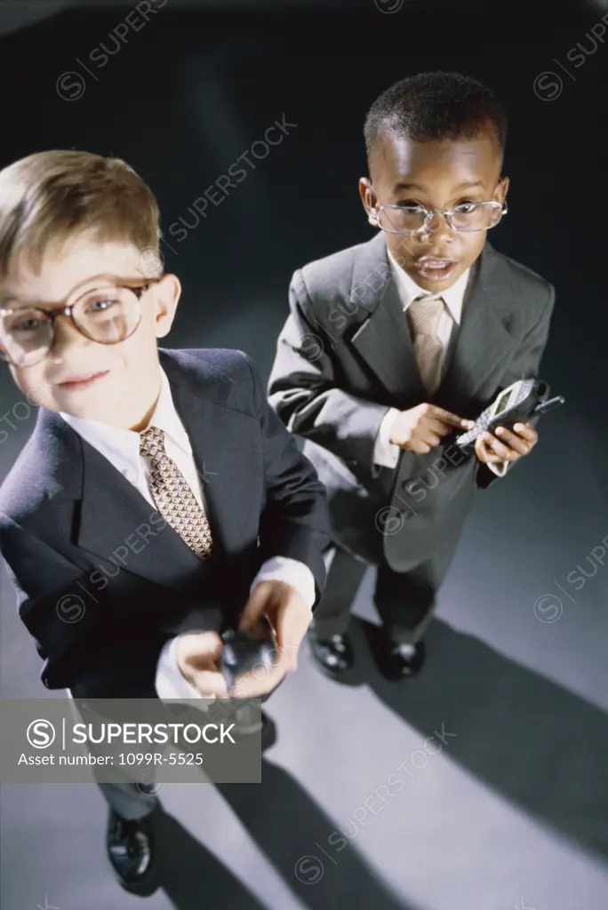 High angle view of two young boys dressed as businessmen operating mobile phones