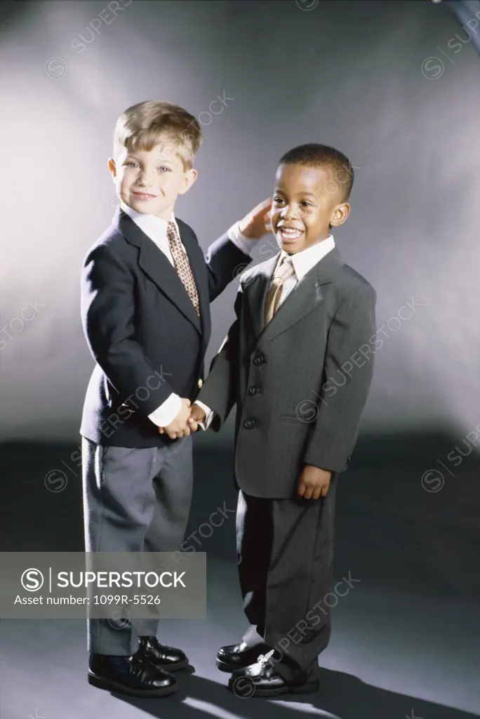 Portrait of two young boys dressed as businessmen shaking hands