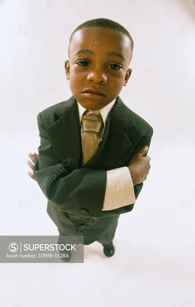 Portrait of a young boy dressed as a businessman standing with his arms folded